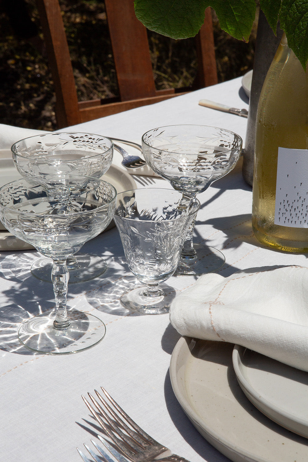 Set table with crystal glasses, silverware, and a bottle of white wine on a white tablecloth.