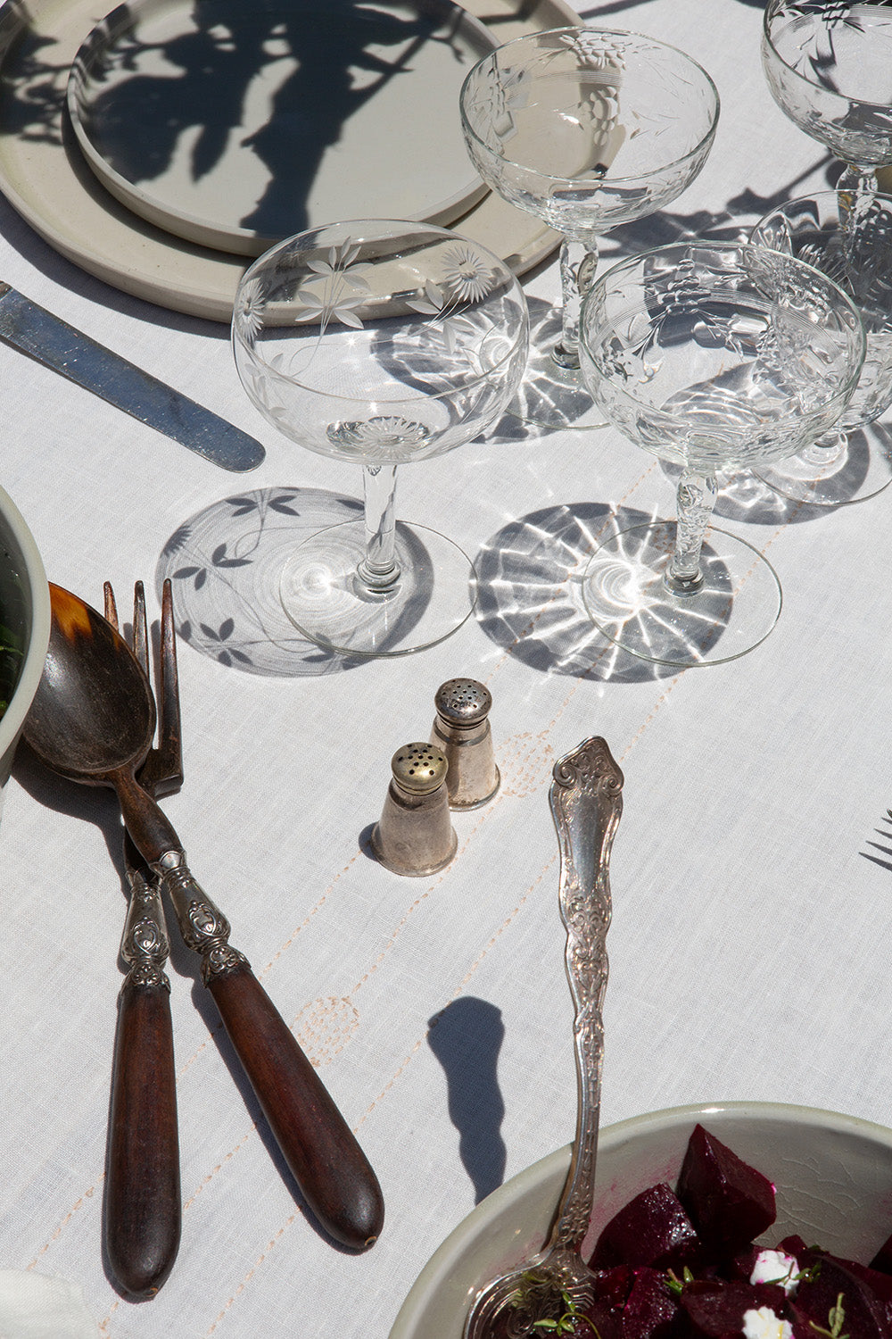 Dining table setting with cutlery, glasses, and salt and pepper shakers on a white tablecloth.